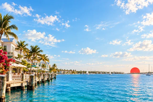 Editorial artwork of an airy Key West waterfront with a red sun and open blue water.